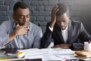 People, business and failure. Two tired and depressed African American businessmen doing paperwork, reviewing accounts, working on financial report together, having stressed and frustrated looks